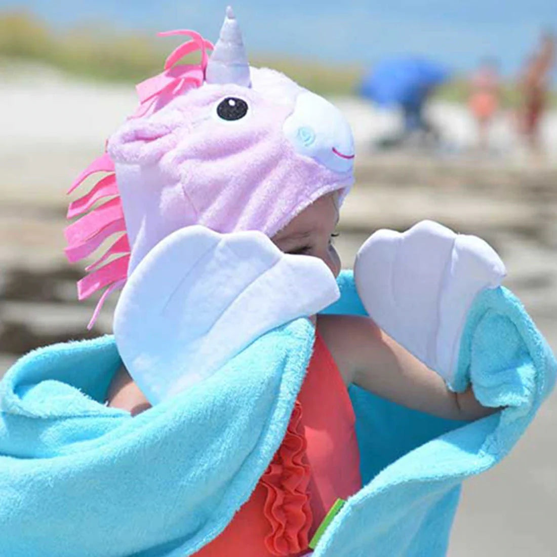Kind op het strand met de eenhoornbadcape, roze manen en handen in de witte vleugels.